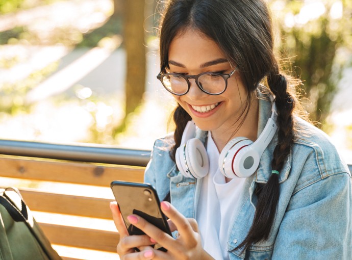 Woman smiling at her phone with headphones around her neck